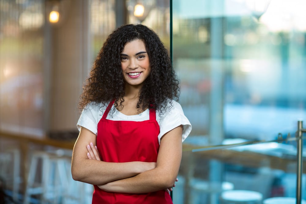 Portrait of smiling waitress standing with arms crossed in cafe